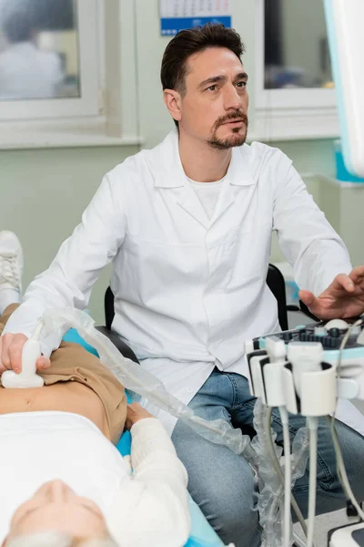 Уважний лікар у білому пальто робить нирки УЗД пацієнта в клініці — стокове фото