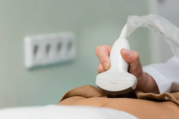 Sonda de ultrasonido en la mano del médico haciendo examen abdominal de la mujer en la clínica - foto de stock