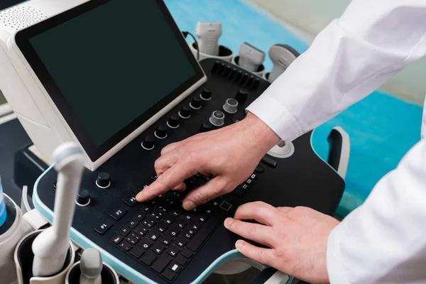 Vue recadrée du médecin en utilisant le panneau de commande de la machine à ultrasons avec écran blanc — Photo de stock