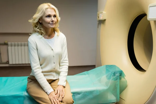 Sorrindo mulher de meia-idade sentado perto tomografia computadorizada scanner na clínica — Fotografia de Stock