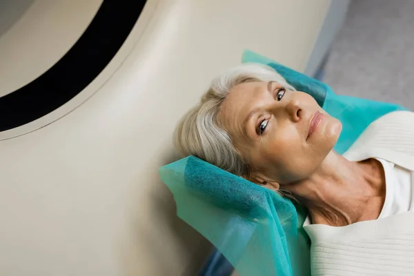 Hochwinkelaufnahme einer blonden Frau mittleren Alters, die während der Untersuchung auf dem CT-Scanner in die Kamera schaut — Stockfoto