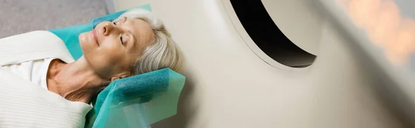 Hochwinkelaufnahme einer reifen Frau mit geschlossenen Augen, die während der Diagnostik auf dem CT-Scanner in der Klinik liegt, Banner — Stockfoto