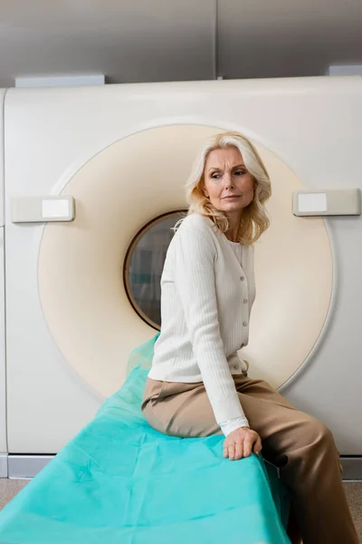 Tenso mulher de meia-idade sentado perto tomografia computadorizada scanner e olhando para longe — Fotografia de Stock