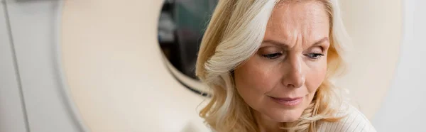 Tense blonde woman near computed tomography scanner in hospital, banner — Stock Photo