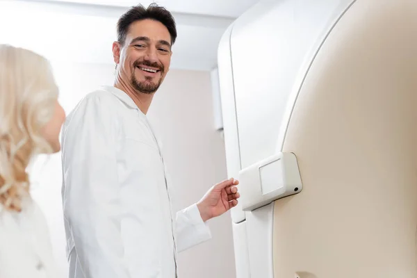 Низький кут зору усміхненого радіолога, який дивиться на розмиту жінку біля комп'ютерної томографічної машини — стокове фото