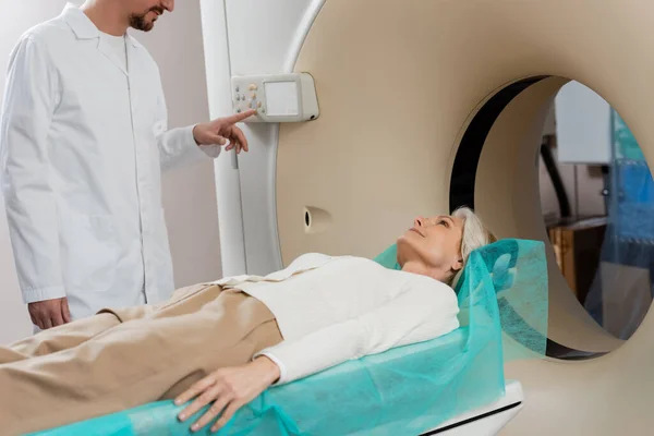 Frau mittleren Alters liegt während der Diagnostik in der Nähe von Arzt, der CT-Scanner operiert — Stockfoto