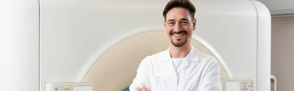 Alegre médico sonriendo a la cámara mientras está de pie cerca del escáner de tomografía computarizada, pancarta - foto de stock