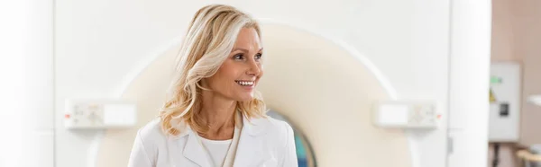 Счастливая блондинка радиолог глядя в сторону компьютерной томографии машины, баннер — стоковое фото