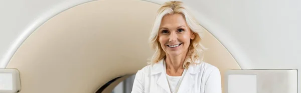 Radiologue d'âge moyen souriant à la caméra près de la machine de tomodensitométrie, bannière — Photo de stock