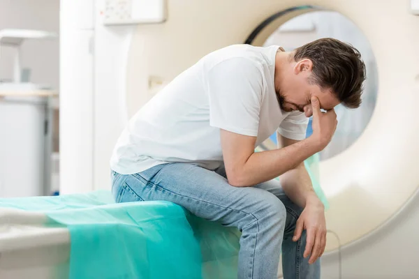Stressed man sitting near ct scanner with bowed head and covering face with hand — Stock Photo