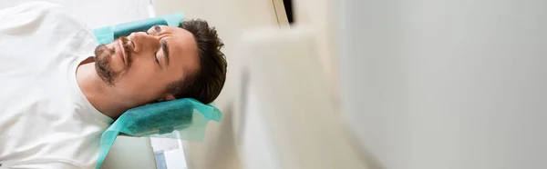 Hombre preocupado con los ojos cerrados haciendo tomografía computarizada en el hospital, bandera - foto de stock