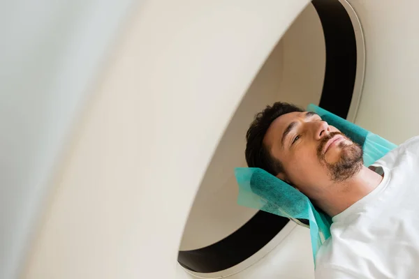 Vue grand angle de l'homme brune couché pendant la numérisation sur machine de tomodensitométrie — Photo de stock