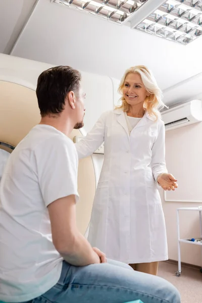 Radiologista sorrindo de meia-idade falando com o homem morena perto tomografia computadorizada scanner — Fotografia de Stock