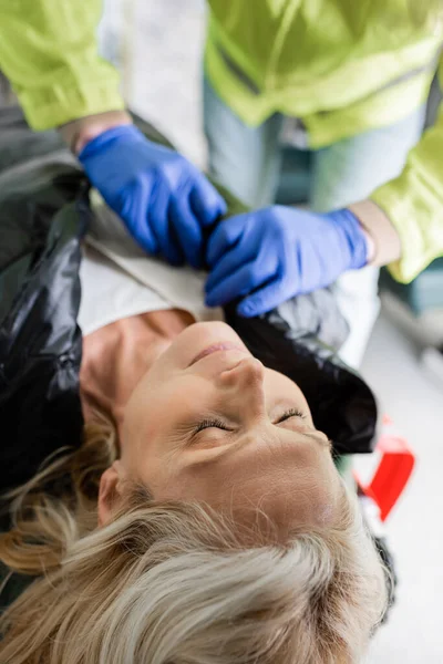Blurred paramedic undressing unconscious middle aged woman in emergency vehicle — Stock Photo