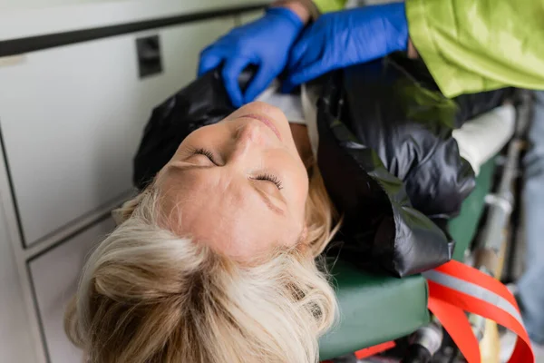 Un ambulancier ambulancier flou enlève la veste d'une femme inconsciente d'âge moyen lors du premier vol dans un véhicule d'urgence — Photo de stock