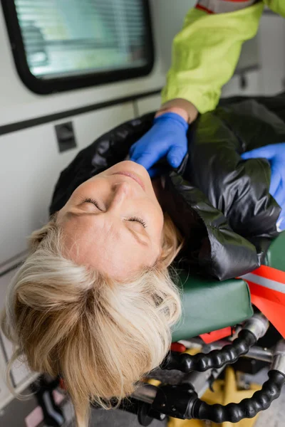 Unconscious woman lying near blurred paramedic in latex gloves in emergency vehicle — Stock Photo
