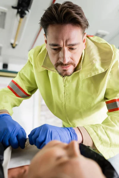 Парамедик в латексных перчатках снимает одежду с размытого пациента в машине скорой помощи — стоковое фото