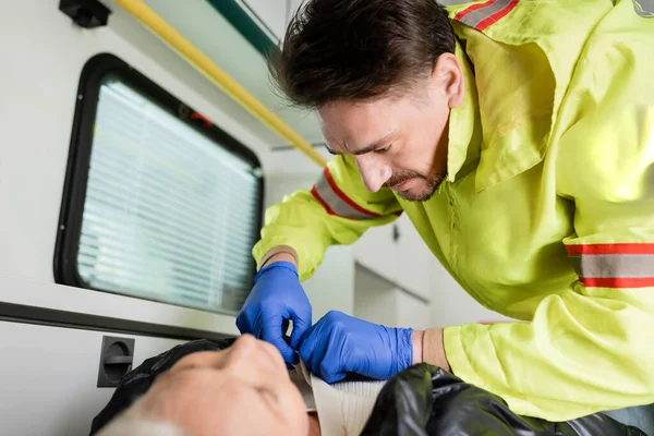 Paramédico en uniforme y guantes de látex quitándose la ropa del paciente durante los primeros auxilios - foto de stock