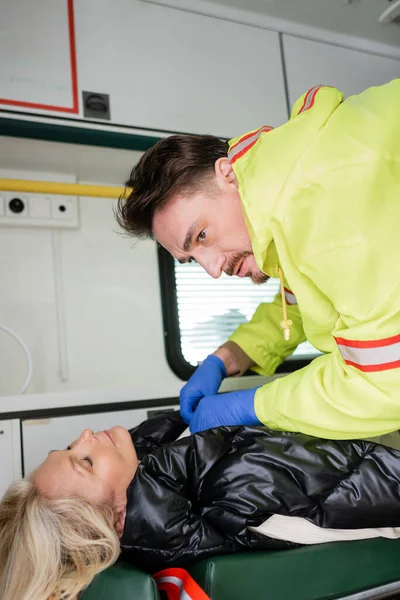 Paramédico em luvas de látex dando primeiros socorros a mulher inconsciente de meia-idade em veículo de emergência — Stock Photo