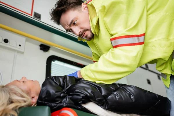 Paramédico de uniforme dando primeiros socorros ao paciente inconsciente em veículo de emergência — Fotografia de Stock
