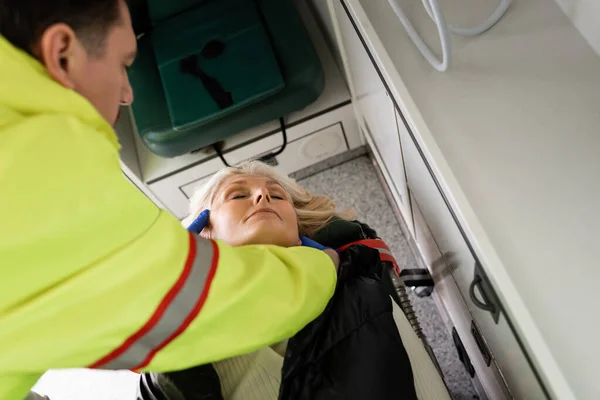 Visão de alto ângulo de paramédico desfocado dando primeiros socorros a mulher madura inconsciente em veículo de emergência — Fotografia de Stock