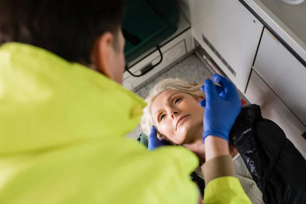 Visão de alto ângulo do paramédico desfocado em luvas de látex que dão primeiros socorros ao paciente em veículo de emergência — Fotografia de Stock