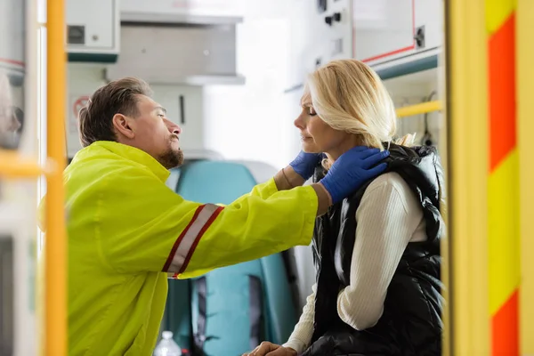 Side view of paramedic in latex gloves checking middle aged patient with hypertension in emergency vehicle — Stock Photo