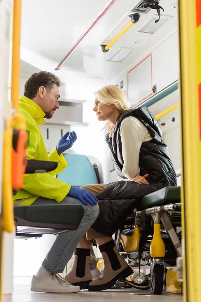 Парамедик в латексных перчатках разговаривает со зрелым пациентом в машине скорой помощи — стоковое фото