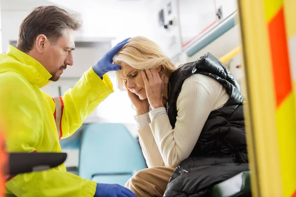 Paramedic in latex gloves touching head of middle aged woman in emergency car — Stock Photo
