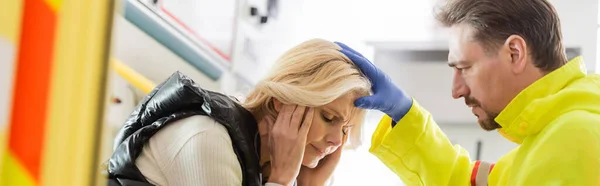 Paramédico en guante de látex tocando la cabeza de la mujer enferma en el coche de emergencia, pancarta — Stock Photo