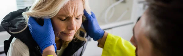 Paramedic checking head of displeased middle aged woman in emergency vehicle, banner — Stock Photo