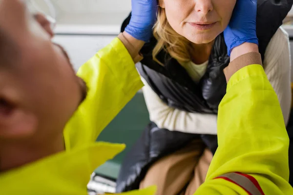 Vue recadrée d'ambulancier paramédical flou dans des gants en latex donnant les premiers soins à une femme d'âge moyen — Photo de stock