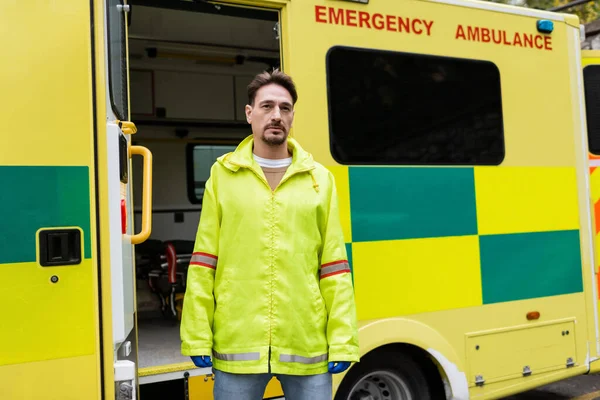 Paramédico en guantes de látex de pie cerca de coche ambulancia al aire libre - foto de stock