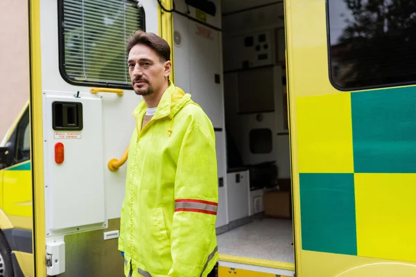 Paramedico in uniforme in piedi vicino ambulanza auto sulla strada urbana — Foto stock