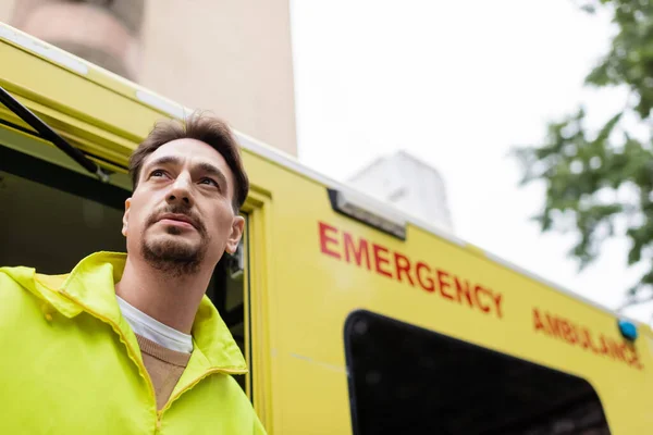 Low angle view of paramedic standing near ambulance vehicle with open door outdoors — Stock Photo