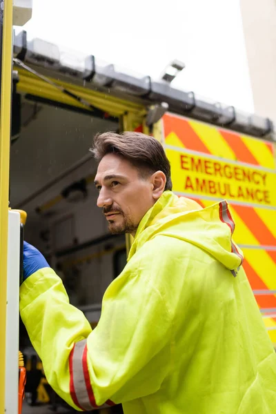 Paramedic in uniform opening door of ambulance car on street — Stock Photo