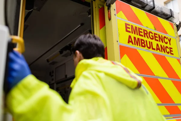 Lettere di emergenza per ambulanze sul veicolo vicino a paramedici sfocati all'aperto — Foto stock