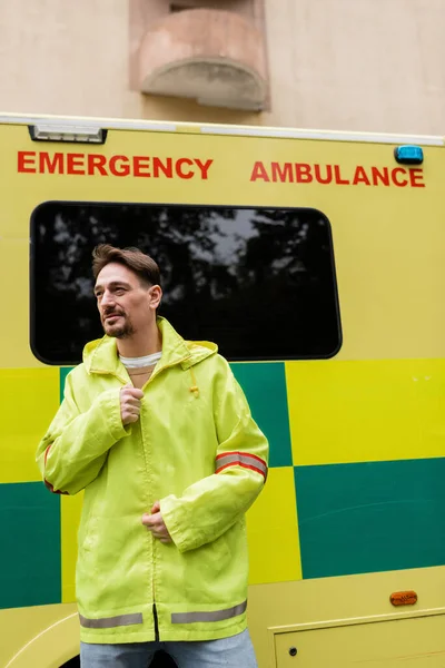 Paramedic wearing jacket near ambulance car on urban street — Stock Photo