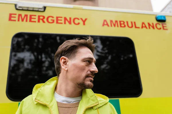 Side view of paramedic looking away near blurred ambulance auto outdoors — Stock Photo