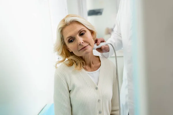 Verschwommener Arzt hält Sonographen am Hals reifer Patientin in Klinik — Stockfoto
