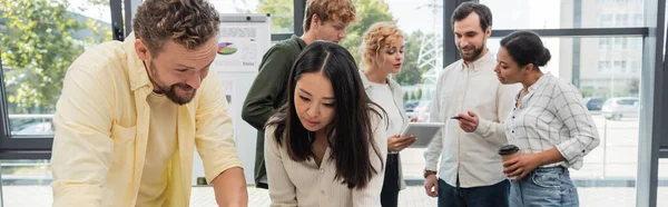 Brunette asian woman near bearded colleague and business team talking on background, banner — Stock Photo