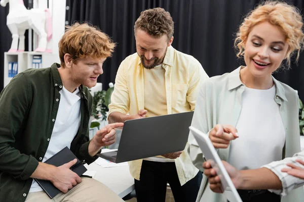 Positive business people pointing at laptop and digital tablet while working in office — Stock Photo