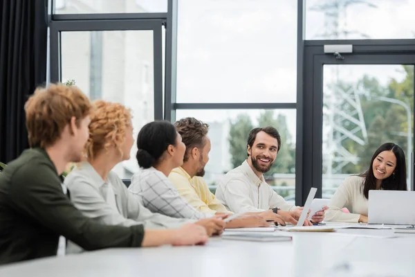 Bearded man and asian woman smiling at interracial business colleagues in meeting room — Stock Photo