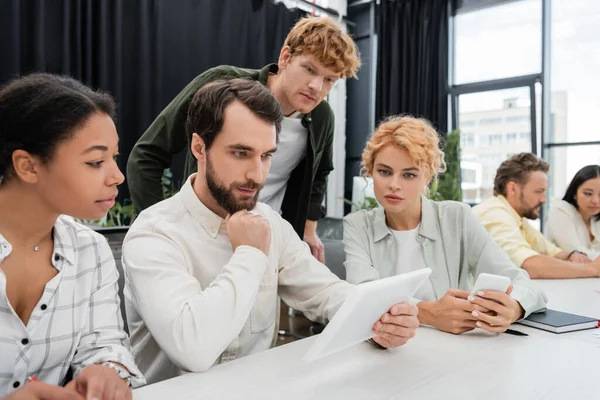 Бородатий бізнесмен дивиться на цифровий планшет під час зустрічі з багатоетнічними колегами — стокове фото