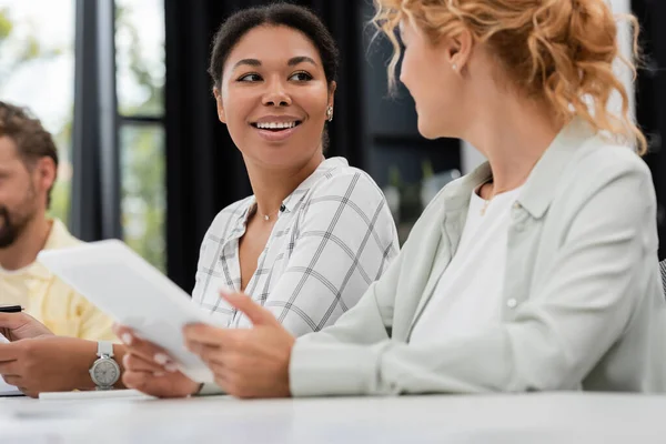 Smiling multiracial businesswoman looking at colleague with digital tablet on blurred foreground — Stock Photo