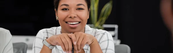 Jeune femme d'affaires multiraciale avec stylo regardant la caméra dans le bureau, bannière — Photo de stock