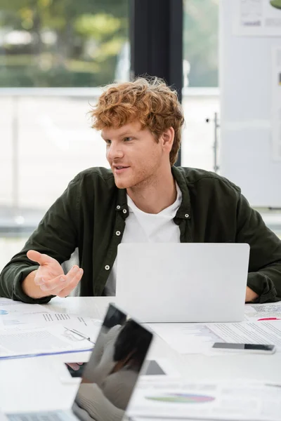 Redhead businessman pointing with hand and talking near laptops in office — Stock Photo