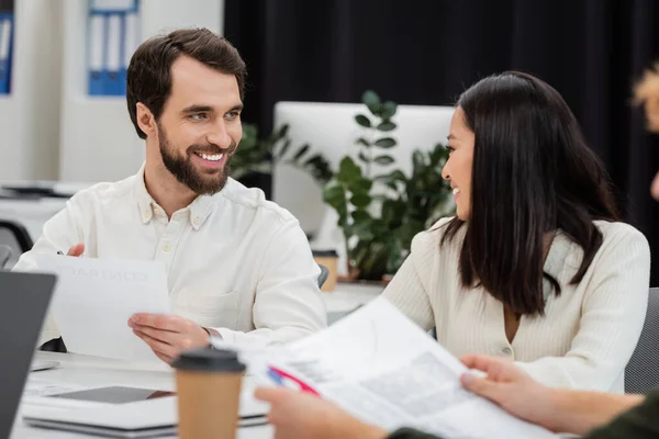 Bearded man with document looking at young asian colleague while working in office — Stock Photo