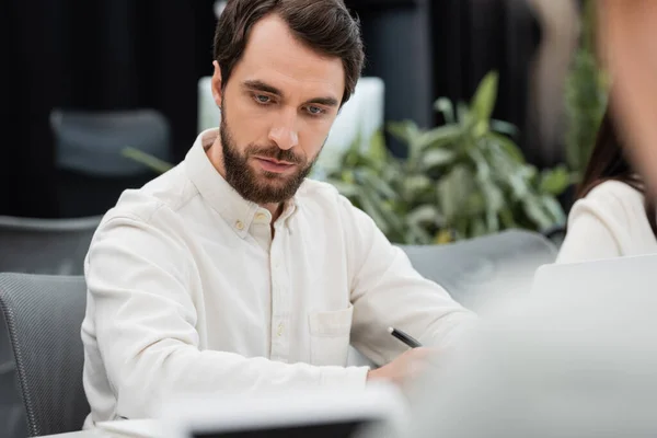 Serious bearded businessman working in office on blurred foreground — Stock Photo