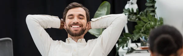 Бородатий бізнесмен сидить руками за головою і посміхається в офісі, банер — стокове фото